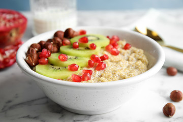 Bowl of quinoa porridge with hazelnuts, kiwi and pomegranate seeds on marble table