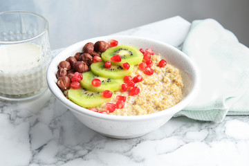 Bowl of quinoa porridge with hazelnuts, kiwi and pomegranate seeds on marble table