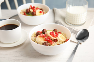 Quinoa porridge with hazelnuts, kiwi, banana and pomegranate seeds served for breakfast on white wooden table