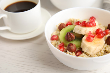 Bowl of quinoa porridge with hazelnuts, kiwi, banana and pomegranate seeds served for breakfast on white wooden table