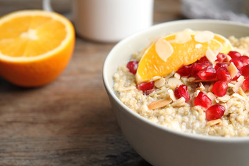 Bowl of quinoa porridge with nuts, orange and pomegranate seeds on wooden table, closeup