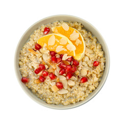 Bowl of quinoa porridge with nuts, orange and pomegranate seeds on white background, top view