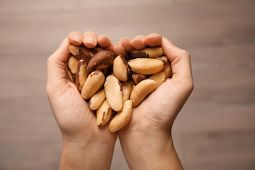Woman holding Brazil nuts in hands on blurred background, top view