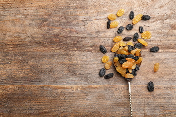 Spoon with raisins and space for text on wooden background, top view. Dried fruit as healthy snack