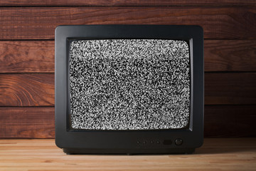 Old vintage TV set televisor on wooden table againt dark wooden wall background with no signal television grainy noise effect on the screen