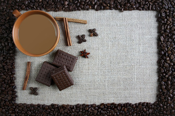 A cup of coffee surrounde by coffee beans, next to cinnamon and chocolate cakes