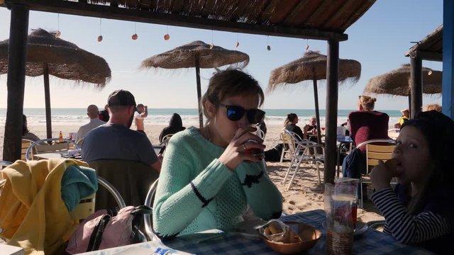 Mother with child daughter sit in Atlantic ocean beach bar eat fried potato and drink tea