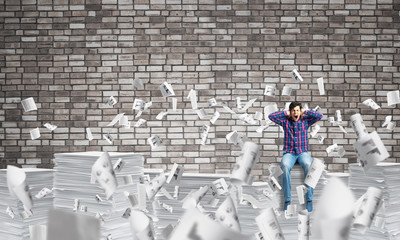 Attractive man sitting on pile of paper documents.