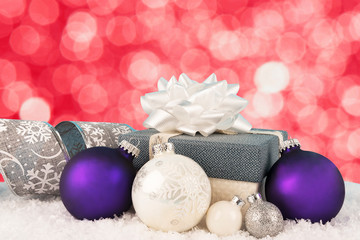 Close up on a Christmas gift box with ribbon and bow. Snow and bauble in decoration. Bokeh lights in background.