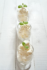 Glasses with a dessert of whipped cream with a fresh mint leaf on a white wooden table.