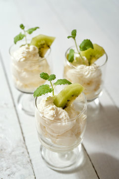 Glass of dessert with whipped cream with a fresh mint leaf and kiwi fruit on white table.