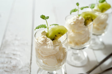 Glass of dessert with whipped cream with a fresh mint leaf and kiwi fruit on white table.
