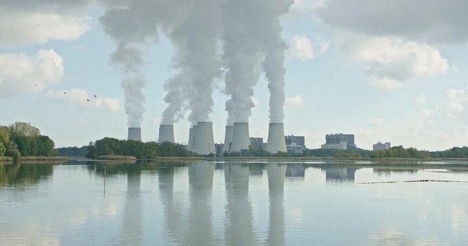 Lignite power plant in front of a lake, birds fly past, the smoke rises steadily in the reflected, an idylic picture of industry and nature
