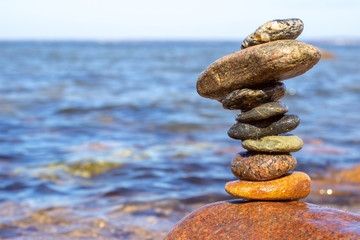 Fototapeta na wymiar Tower of wet stones on sea beach background in summer day