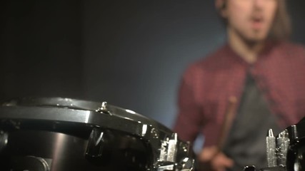 Long-haired drummers play drum kit in a dark room on a black background. Rock musician. Static plan. Wide angle