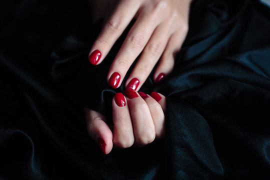 Gorgeous manicure, clssic red color nail polish, closeup photo. Female hands over dark fur background
