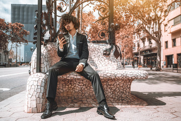 An arrogant bearded Asian guy with curly hair and in a business suit is using his smartphone to see...