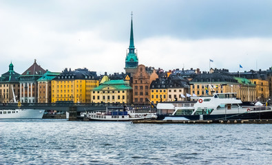 Panoramic view from the boat on waterfront houses in Gamla Stan, tourist boats and Skeppsholmsbron (Skeppsholm Bridge) with Golden Crown in Stockholm Sweden