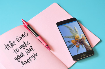 Text about travel in pink notebook, photo in smartphone on blue background, flat lay. Blogging concept, smm. summer vacation
