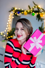 Beautiful woman in red sweater holding a gift box. Makeup mirror on background