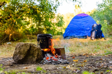 Cooking food in a kettle on bonfire. Tent on background