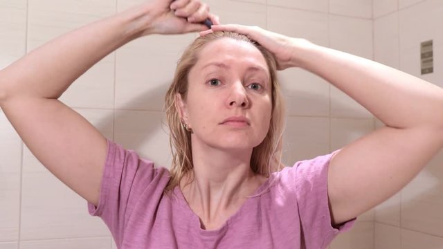 Middle aged blond woman brushing her wet hair with a hair brusher in bathroom