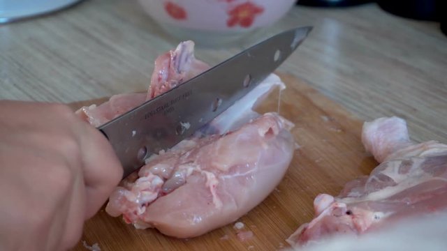 Cut the chicken carcass. Knife in hand. Plucked and gutted chicken. Wooden table. Kitchen interior. Largest species. Daylight. 4K video.