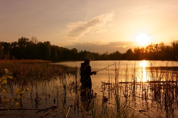 angler standing in a lake and catching the fish during sunset