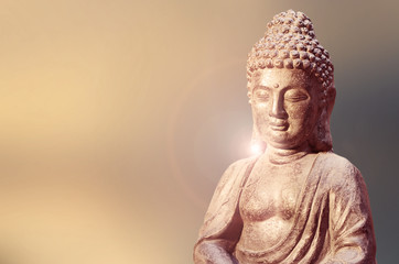 Buddha statue sitting in meditation pose against blurred background.