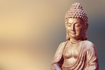 Buddha statue sitting in meditation pose against blurred background.