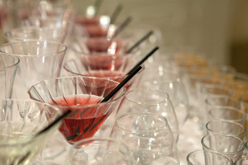 Beautiful row line of different colored alcohol cocktails on a party, martini, vodka,and others on decorated catering bouquet table on open air event, picture with beautiful bokeh