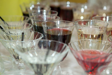 Beautiful row line of different colored alcohol cocktails on a party, martini, vodka,and others on decorated catering bouquet table on open air event, picture with beautiful bokeh