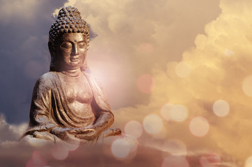 Boeddhabeeld zittend in meditatie pose tegen avondrood met gouden tinten wolken.