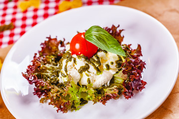 Italian burrata cheese served with cherry tomato, pesto sauce and lettuce leaves on white plate. Close up