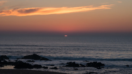 Last sliver of sun setting beneath horizon over ocean from beach