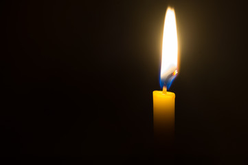 A single candle light glowing on a yellow candle on black background