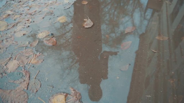 In the puddle on the street is reflected the girl in the coat. The girl looks in reflection smiling and laughing (slow)