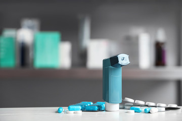 Asthma inhaler and pills on table against blurred background. Space for text