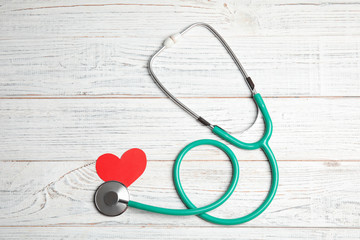 Stethoscope and red heart on wooden background, top view. Cardiology concept
