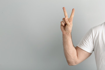 Young man showing victory gesture on light background. Space for text