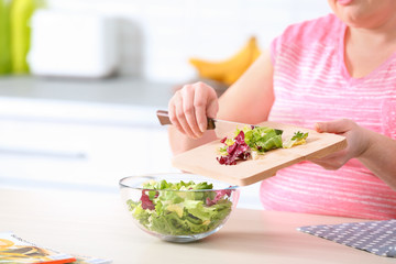 Obraz na płótnie Canvas Overweight woman preparing salad in kitchen, space for text. Healthy diet