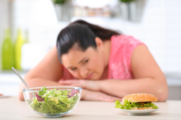 Salad and burger with blurred overweight woman on background. Healthy diet