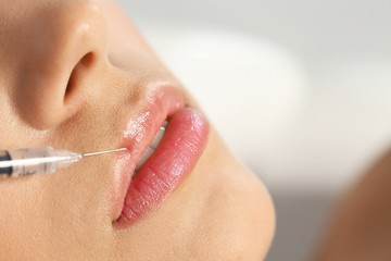 Young woman getting lips injection on blurred background, space for text. Cosmetic surgery