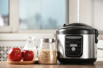 Modern multi cooker and products on table in kitchen. Space for text