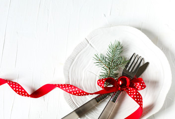 Fork and knife tied with a red ribbon and Christmas decor on white background with copy space. Food, restaurant and table setting theme