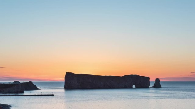 Timelapse, time lapse of Rocher Perce rock in Gaspe Peninsula, Quebec, Gaspesie region, Canada in morning dawn, before sunrise with clear sky at Saint Lawrence gulf, wharf, dock, pier, lighthouse