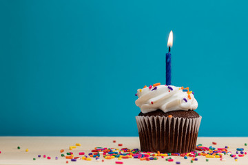 Chocolate Cupcake with candle and sprinkles on a blue background, with room for text 