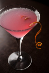 Bright pink cosmopolitan drink served with orange swirl hanging out the side of the glass.