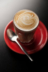 Lovely latte macchiato served on red saucer on a bar top setting