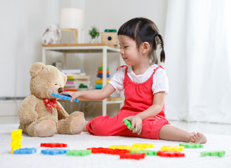 Preschooler girl learns at school. Cute child playing with teddy bear. Little girl having fun indoors at home, kindergarten or